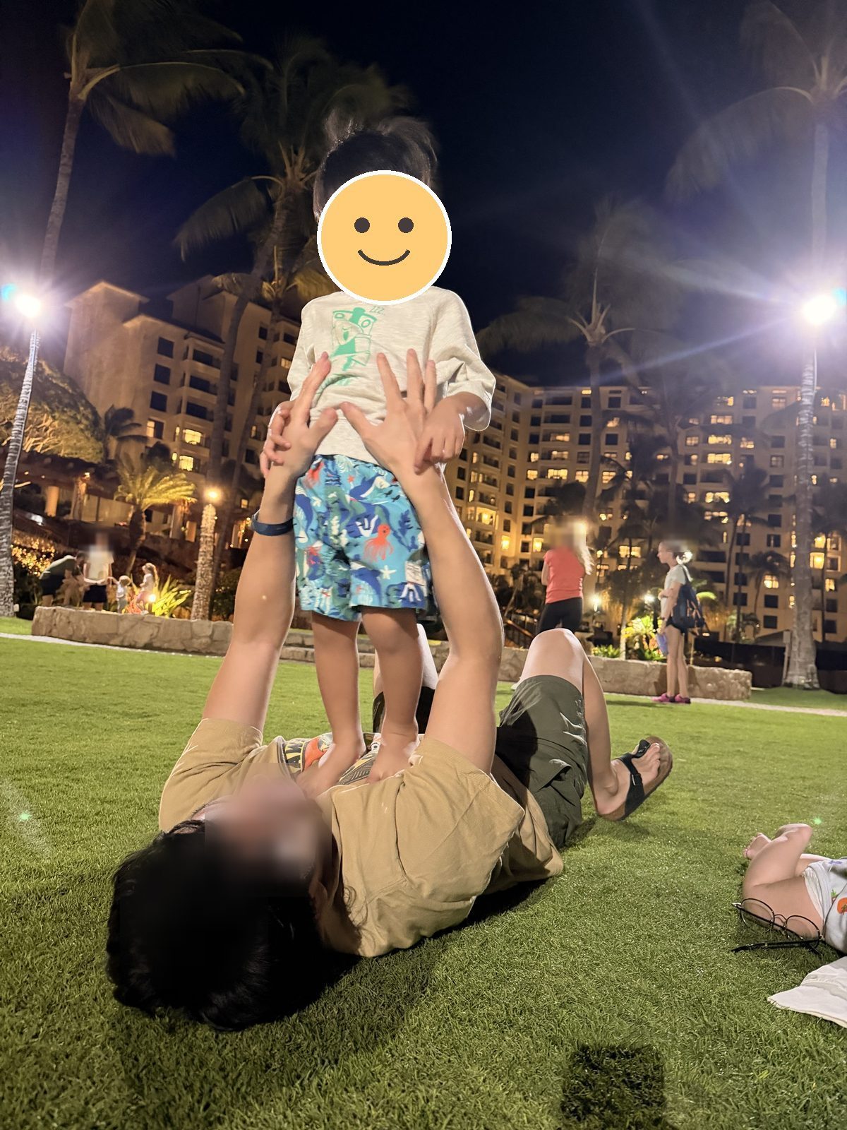 夜の芝生で、寝転んだ大人の上に立つ息子